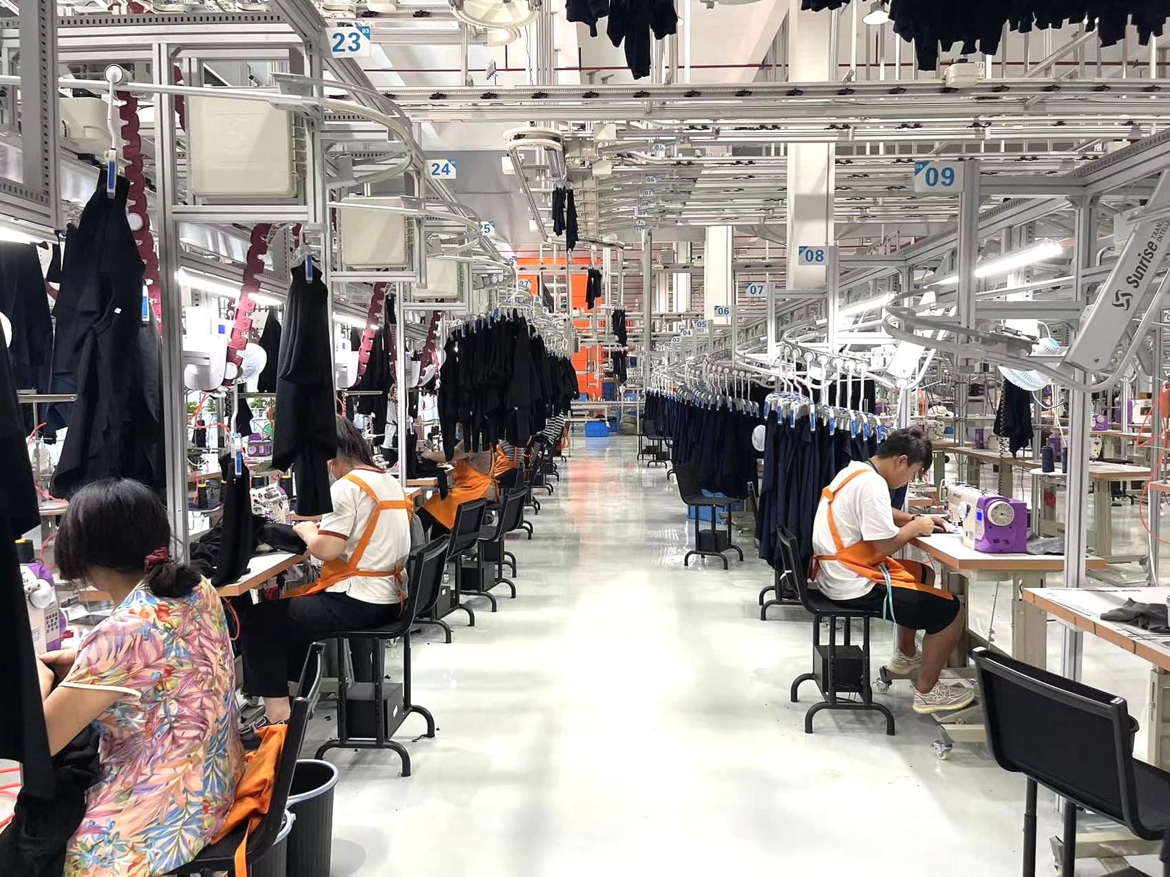 Factory staff sewing garments on a real production floor with an overhead hanging-line system
