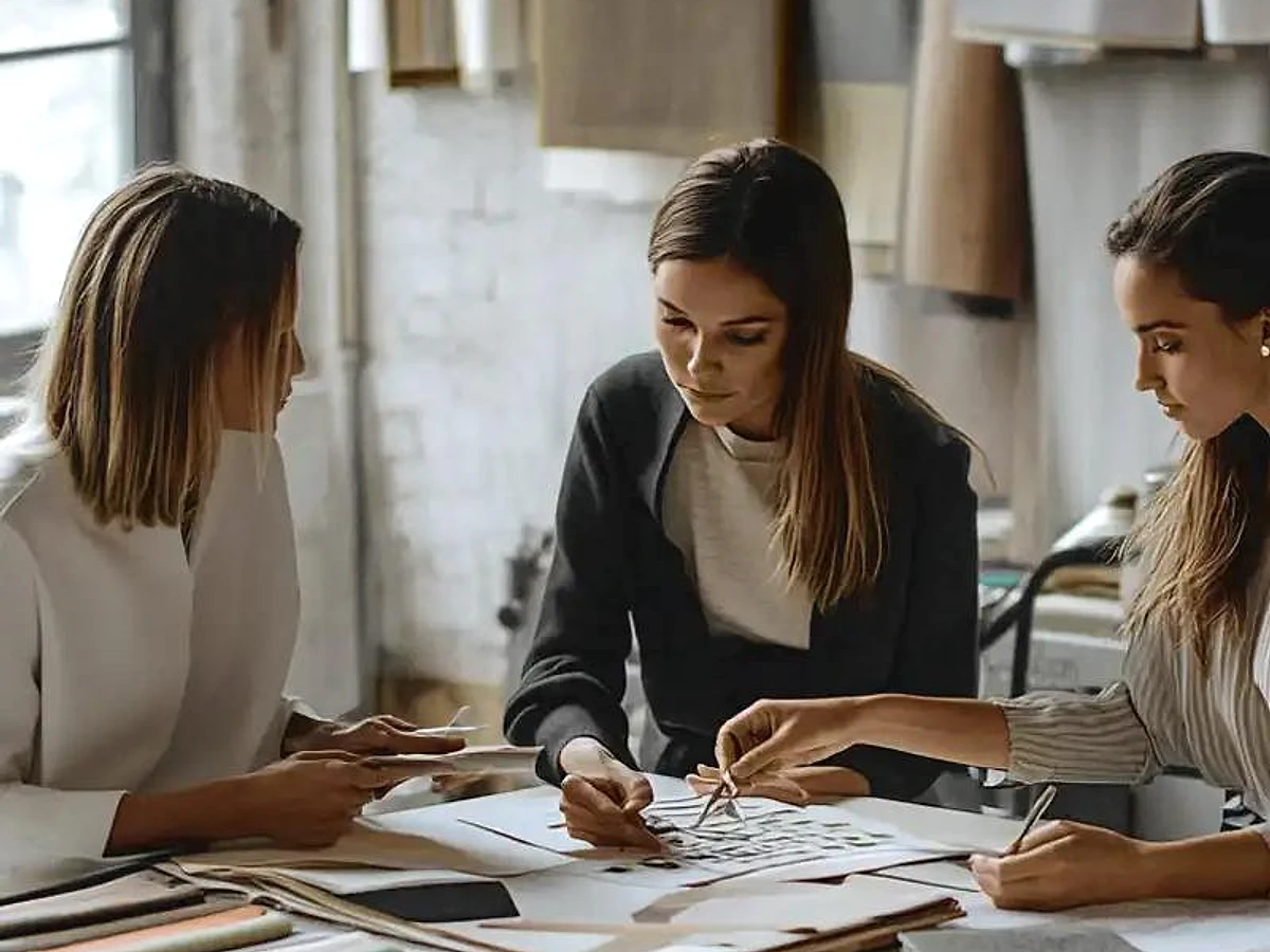 Fashion design team comparing fabric swatches and collection references around a worktable.